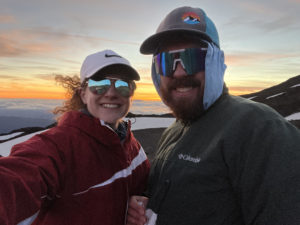 Two people on a mountain with sunset behind